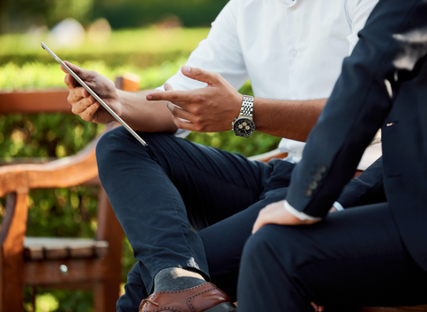 close up of two people sitting on benches outside and gesturing to an electronic tablet
